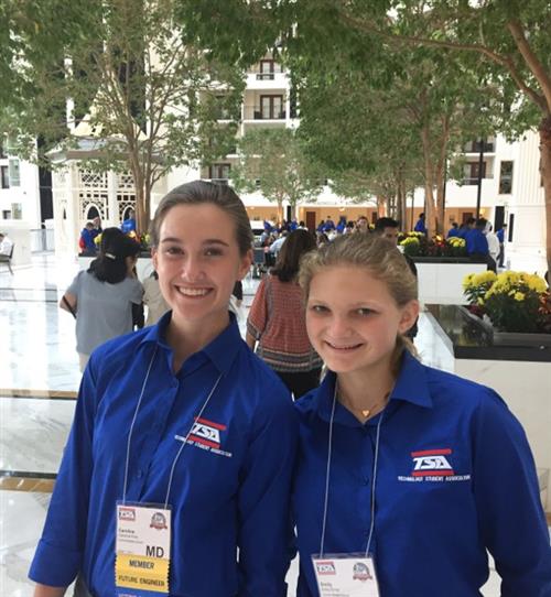 Two girls standing in front of building for TSA competition. Girls smiling wearing blue TSA uniform. 