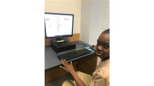 A student sits at a desktop computer which has his Scratch program on the screen. 