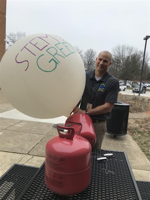 Man is using helium to inflate a weather balloon that reads STEM & Green Expo. 