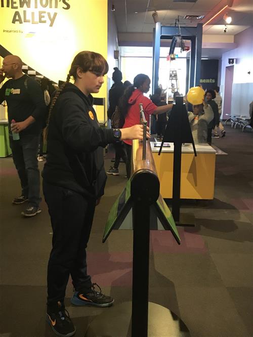 Students at the Maryland Science Center. Girl in front is working a machine at Newton's Alley to learn physics. 