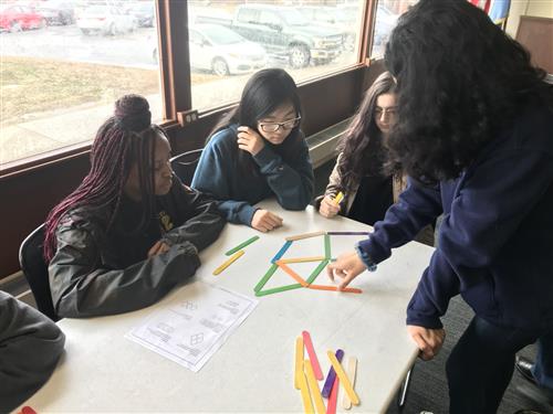 Group of girls sitting at a table move colored sticks to make a pattern from a math workshop at the NSA museum. 