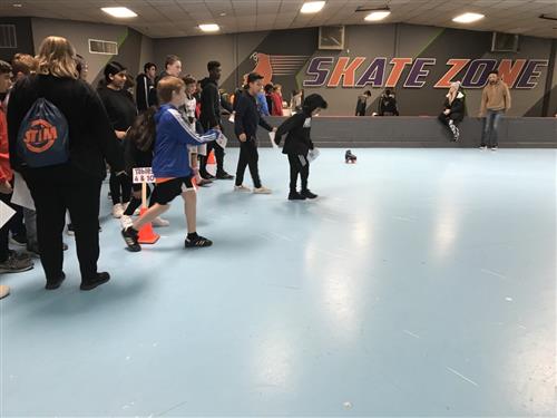 Students line up at Skate Zone to test out friction in roller skates as they push skates along the skating rink floor. 