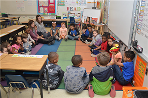 Students in classroom sitting in circle interacting with teacher 