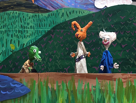 School play depicting colorful characters - a rabbit, gator, and character with white hair against a nature background 