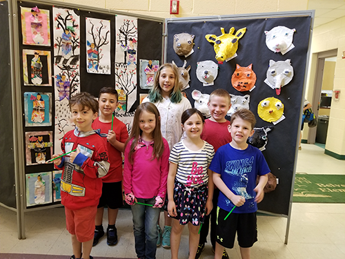 students posting in front of artwork - colorful pictures and animal face depictions 