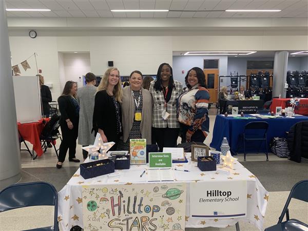 The administrative staff of Hilltop Elementary School posing in front of their table at a job fair. The administrative staff of Hilltop Elementary School posing in front of their table at a job fair.