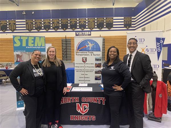 The administrative staff of North County High School posing in front of their table at a job fair. The administrative staff of North County High School posing in front of their table at a job fair.