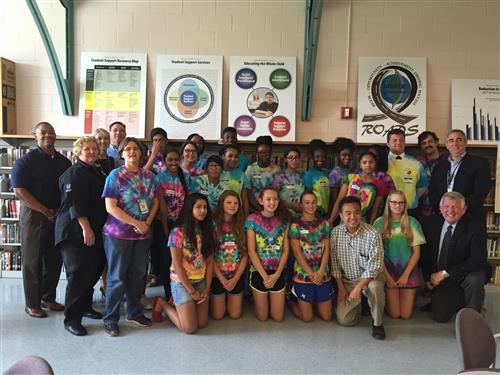 Students wearing tie dye shirts standing with Administrators in front of a bookcase 